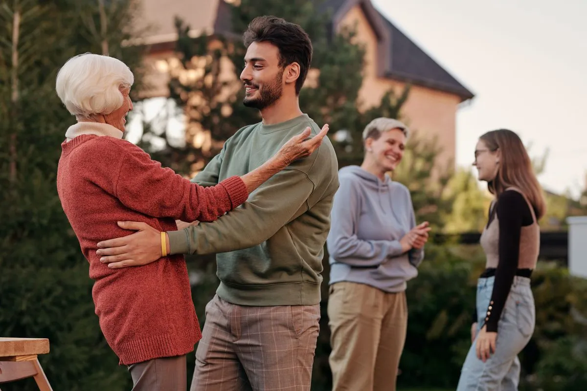 A grown son hugging his mother in the garden, family behind them